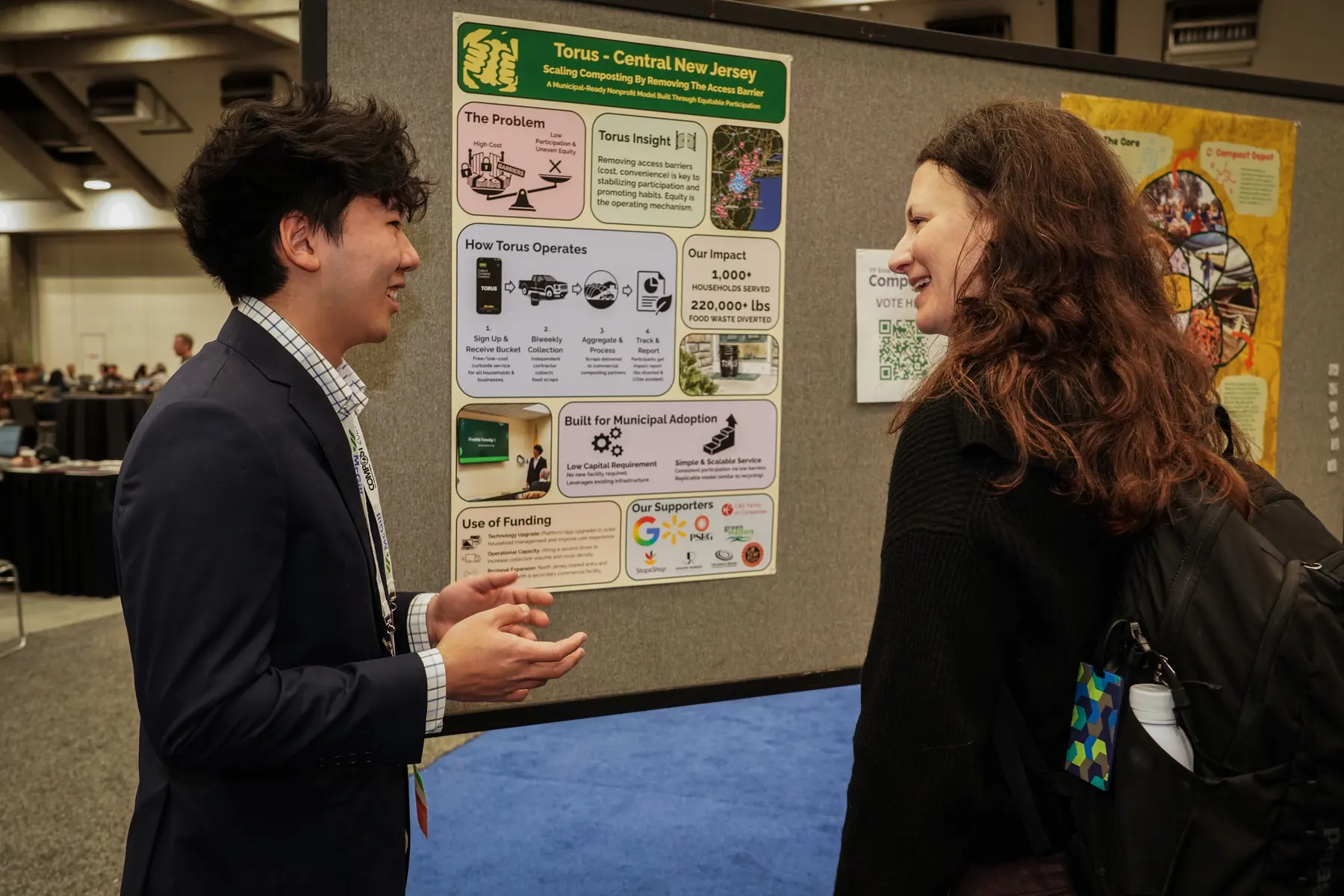 Anthony Woo presenting Torus to a community member beside a Torus composting poster display